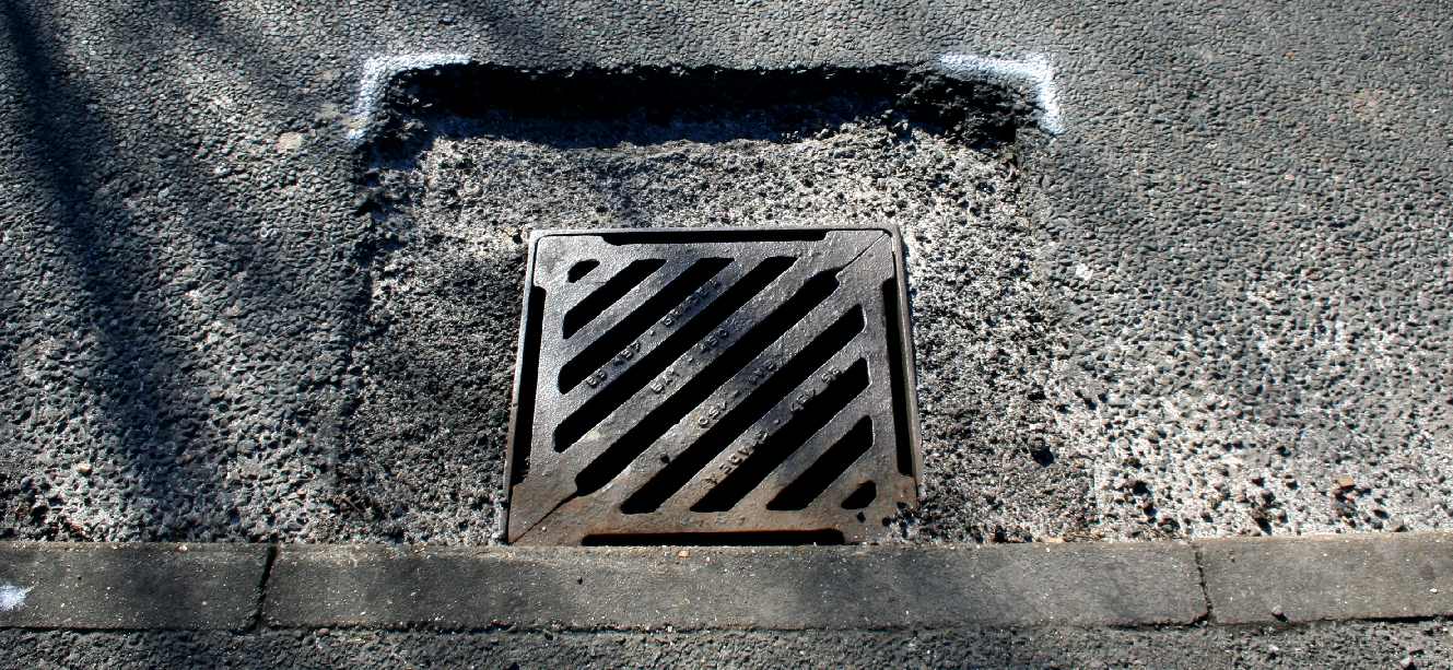 Dangerous cratering around a roadside drain marked for repair